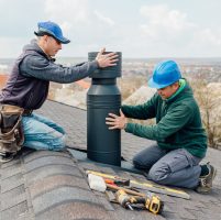 two Professional workmen's standing roof top and measuring chimney of new house under construction against blue background