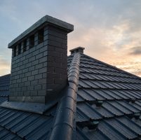 Chimney on house roof top covered with metallic shingles under construction. Tiled covering of building. Real estate development.